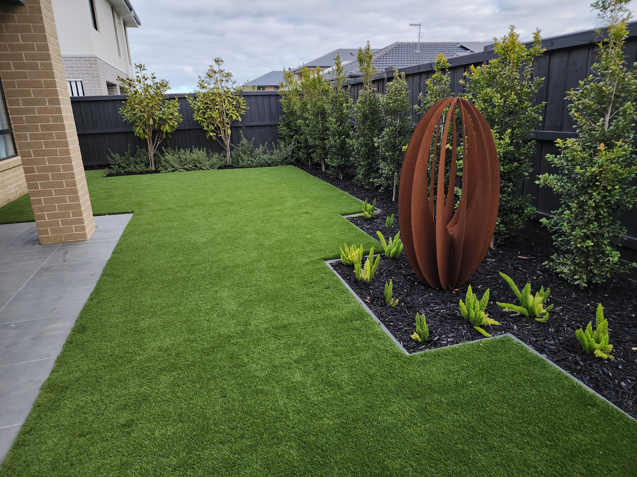 Maintained garden with lawn, layered planting and a steel garden feature